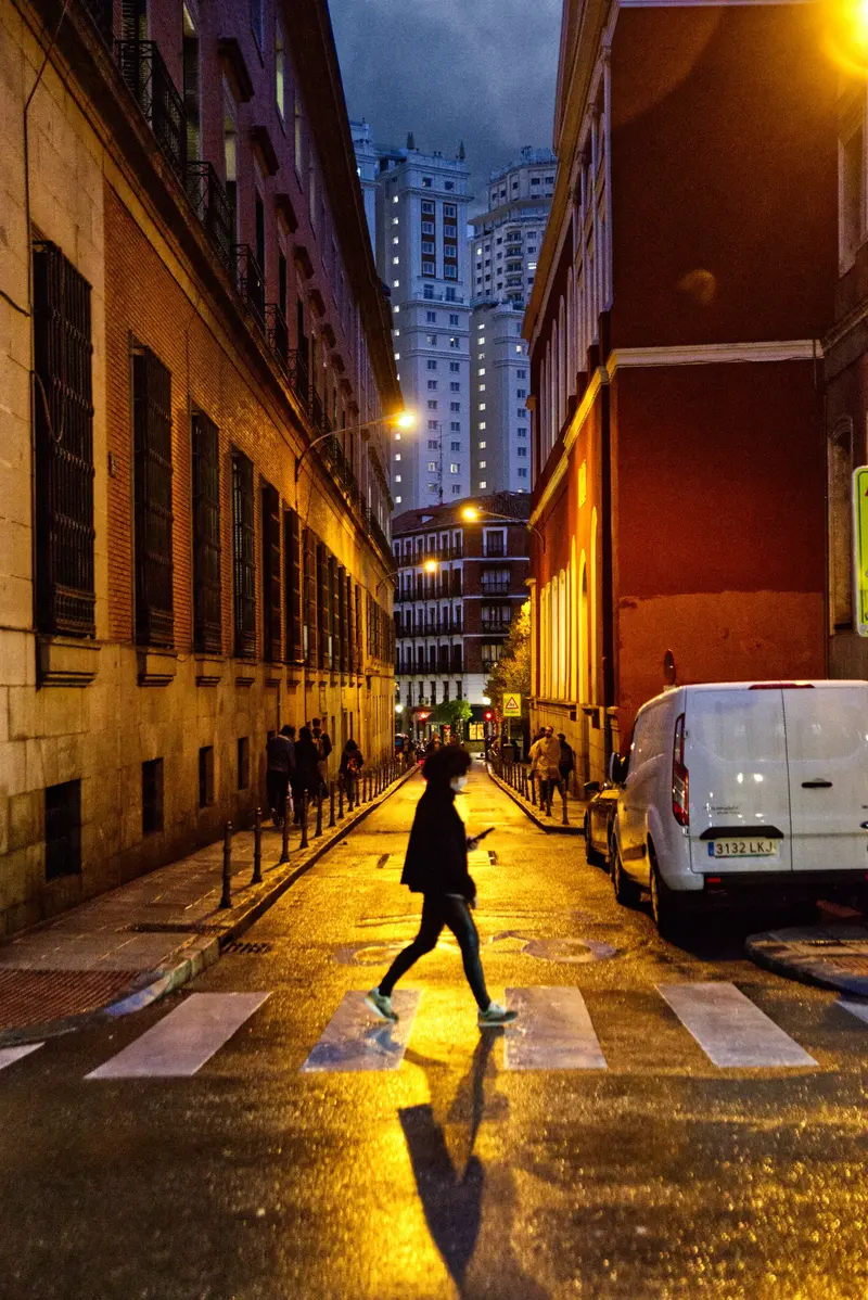 Eine Person überquert nachts eine nasse, schmale Straße in Madrid.