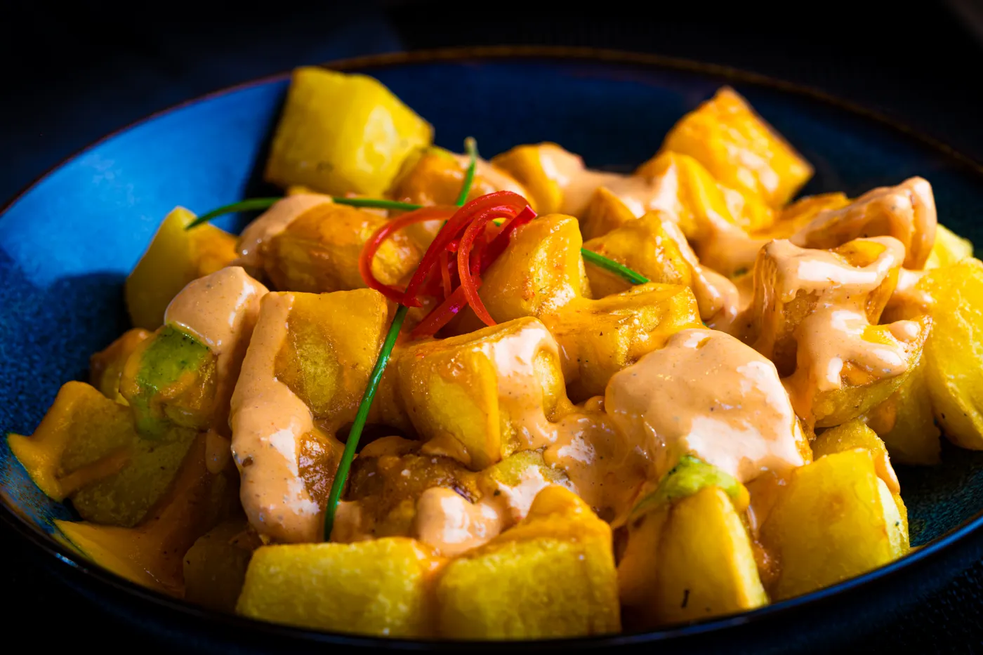 Knusprige Patatas bravas in einer dunkelblauen Keramikschale.