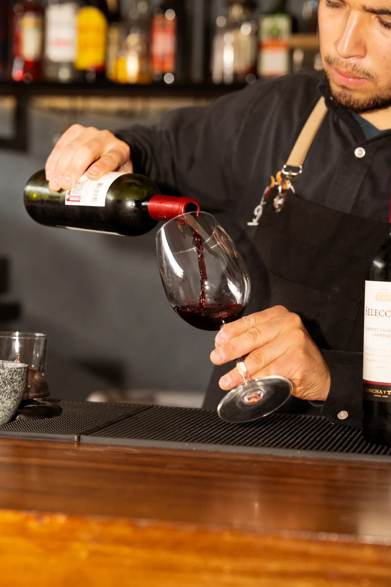Ein Barkeeper schenkt Rotwein konzentriert in ein Glas ein.
